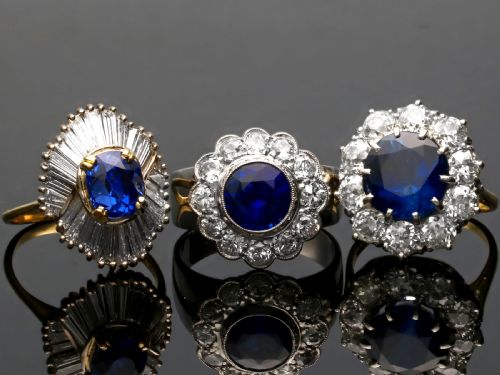 fig 6. A vintage 18ct white gold cluster ring set with a central round blue sapphire surrounded by a halo of brilliant diamonds with a scalloped edge.