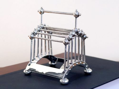 fig 4. An Edwardian sterling silver toast rack featuring a curved base and fan-shaped radiating dividers topped with spherical details.