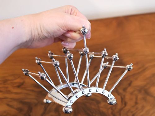 fig 6. An Edwardian sterling silver toast rack featuring a curved base and fan-shaped radiating dividers topped with spherical details.