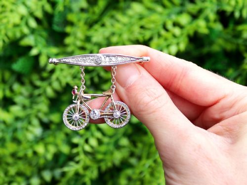 fig 1. An antique Edwardian bar brooch featuring a suspended yellow gold bicycle with diamond-set wheels, set beneath a platinum-faced bar set with diamonds.