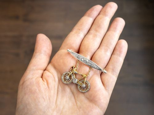 fig 2. An antique Edwardian bar brooch featuring a suspended yellow gold bicycle with diamond-set wheels, set beneath a platinum-faced bar set with diamonds.
