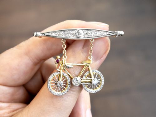 fig 3. An antique Edwardian bar brooch featuring a suspended yellow gold bicycle with diamond-set wheels, set beneath a platinum-faced bar set with diamonds.