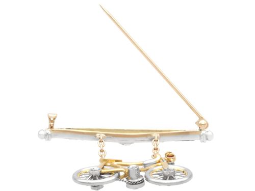 fig 6. An antique Edwardian bar brooch featuring a suspended yellow gold bicycle with diamond-set wheels, set beneath a platinum-faced bar set with diamonds.