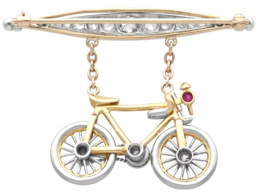 fig 7. An antique Edwardian bar brooch featuring a suspended yellow gold bicycle with diamond-set wheels, set beneath a platinum-faced bar set with diamonds.