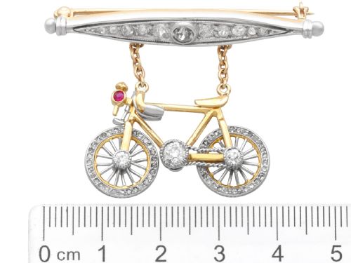fig 8. An antique Edwardian bar brooch featuring a suspended yellow gold bicycle with diamond-set wheels, set beneath a platinum-faced bar set with diamonds.