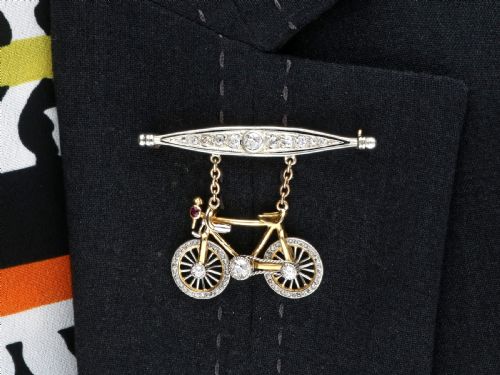 fig 9. An antique Edwardian bar brooch featuring a suspended yellow gold bicycle with diamond-set wheels, set beneath a platinum-faced bar set with diamonds.