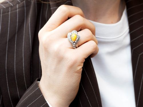 fig 3. A platinum dress ring featuring a central pear-shaped orange opal surrounded by a halo of round and baguette-cut diamonds in an asymmetrical frame.