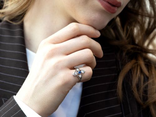 fig 3. An Art Deco 14ct yellow gold ring featuring a central oval blue sapphire surrounded by four round diamonds set in a diamond-shaped openwork frame.