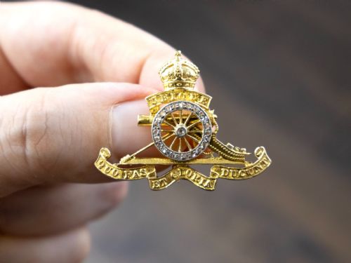 fig 3. An 18ct yellow gold Royal Artillery brooch featuring a diamond-set gun wheel, crowned cannon motif, and Latin motto ribbons.