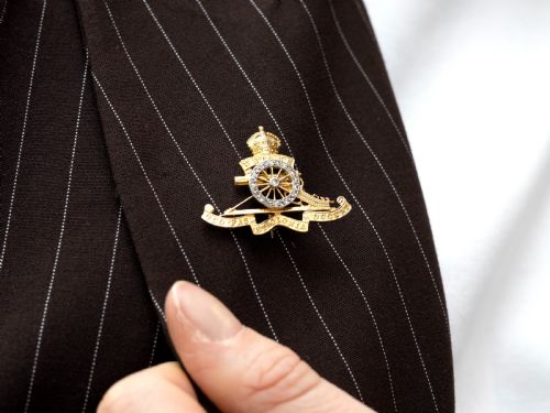 fig 4. An 18ct yellow gold Royal Artillery brooch featuring a diamond-set gun wheel, crowned cannon motif, and Latin motto ribbons.