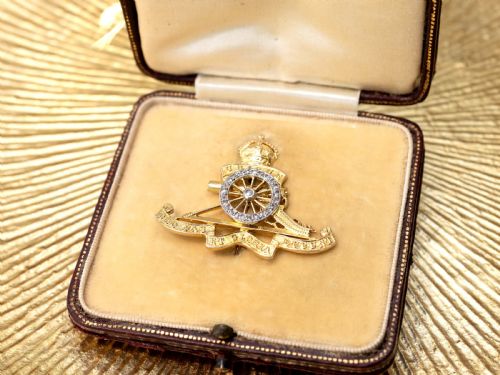 fig 5. An 18ct yellow gold Royal Artillery brooch featuring a diamond-set gun wheel, crowned cannon motif, and Latin motto ribbons.