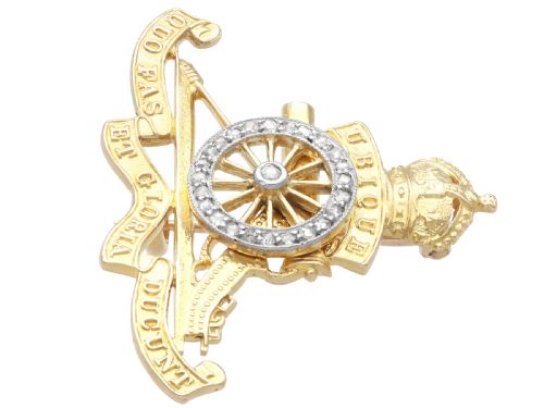 fig 7. An 18ct yellow gold Royal Artillery brooch featuring a diamond-set gun wheel, crowned cannon motif, and Latin motto ribbons.