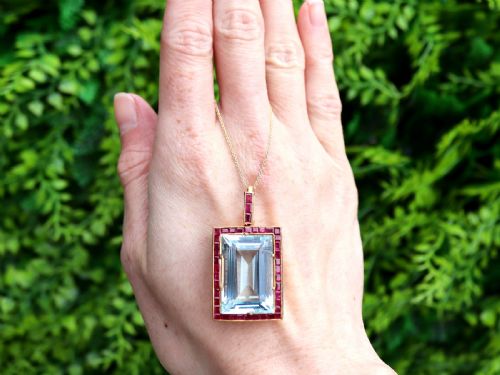 fig 1. A large rectangular step-cut blue aquamarine set in yellow gold with a square-cut red ruby border and ruby-set bail.