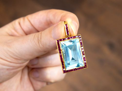 fig 2. A large rectangular step-cut blue aquamarine set in yellow gold with a square-cut red ruby border and ruby-set bail.