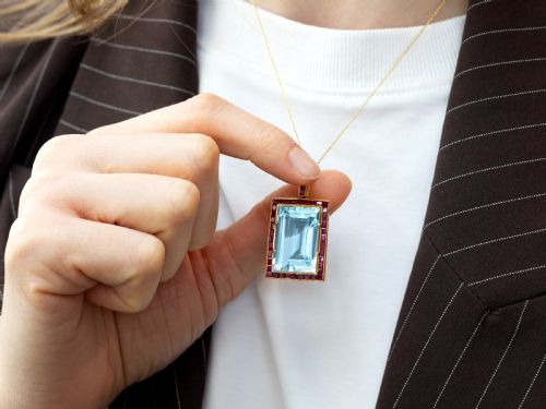 fig 3. A large rectangular step-cut blue aquamarine set in yellow gold with a square-cut red ruby border and ruby-set bail.