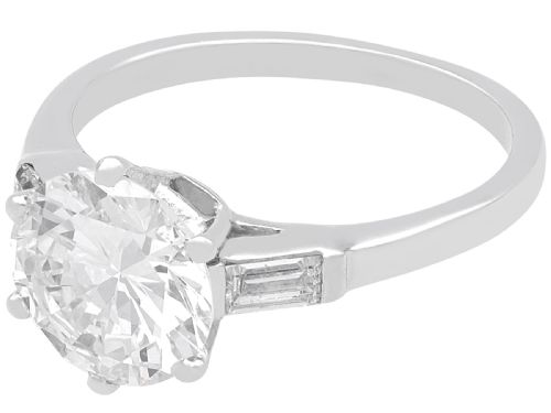 fig 4. A platinum solitaire ring featuring a large round cut central diamond set with six claws, flanked by step-cut baguette diamonds on each shoulder.