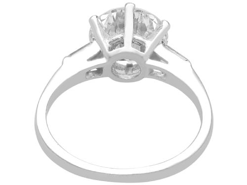 fig 5. A platinum solitaire ring featuring a large round cut central diamond set with six claws, flanked by step-cut baguette diamonds on each shoulder.