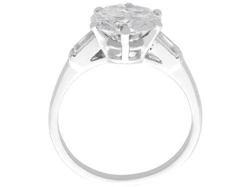 fig 6. A platinum solitaire ring featuring a large round cut central diamond set with six claws, flanked by step-cut baguette diamonds on each shoulder.