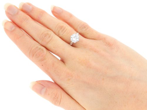 fig 7. A platinum solitaire ring featuring a large round cut central diamond set with six claws, flanked by step-cut baguette diamonds on each shoulder.