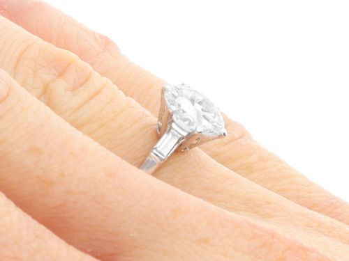 fig 8. A platinum solitaire ring featuring a large round cut central diamond set with six claws, flanked by step-cut baguette diamonds on each shoulder.