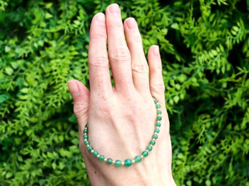fig 2. An antique single strand necklace displaying alternating green emerald beads and cream pearls connected to a geometric platinum and diamond clasp.