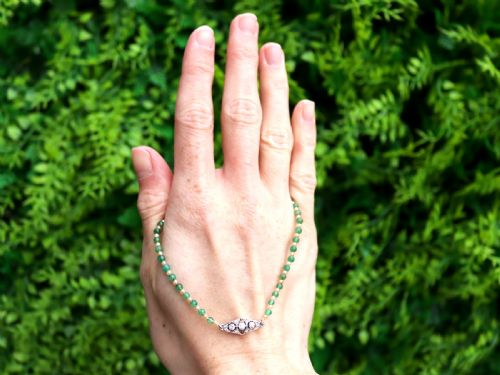 fig 3. An antique single strand necklace displaying alternating green emerald beads and cream pearls connected to a geometric platinum and diamond clasp.