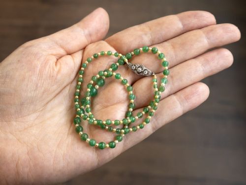 fig 7. An antique single strand necklace displaying alternating green emerald beads and cream pearls connected to a geometric platinum and diamond clasp.