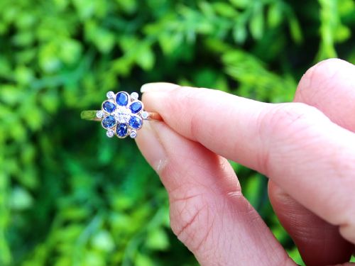 fig 1. An 18ct yellow gold ring featuring a central round diamond surrounded by six oval blue sapphires and outer round diamond accents arranged in a flower motif.