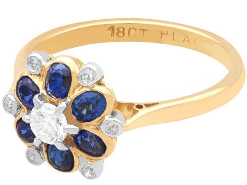 fig 5. An 18ct yellow gold ring featuring a central round diamond surrounded by six oval blue sapphires and outer round diamond accents arranged in a flower motif.