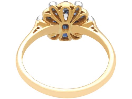 fig 6. An 18ct yellow gold ring featuring a central round diamond surrounded by six oval blue sapphires and outer round diamond accents arranged in a flower motif.