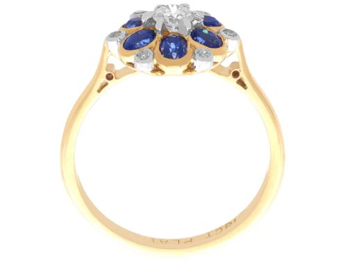fig 7. An 18ct yellow gold ring featuring a central round diamond surrounded by six oval blue sapphires and outer round diamond accents arranged in a flower motif.