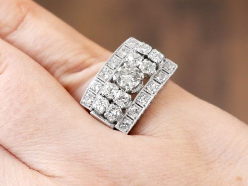 fig 2. An Art Deco platinum dress ring featuring a central round diamond bordered by multiple smaller old-cut diamonds in a geometric rectangular mount with millegrain edges.