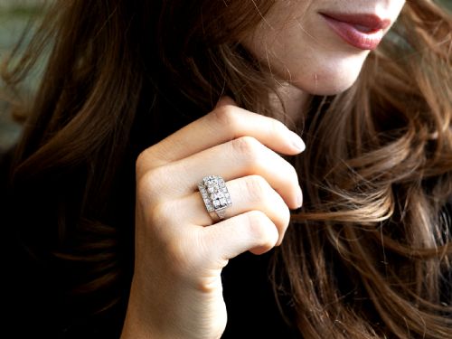 fig 1. An Art Deco platinum dress ring featuring a central round diamond bordered by multiple smaller old-cut diamonds in a geometric rectangular mount with millegrain edges.