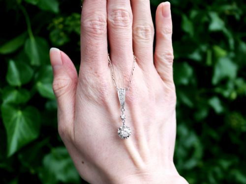 fig 1. An Art Deco platinum drop pendant set with diamonds, featuring a decorative tapered top bail and suspended circular diamond setting on a fine link chain.