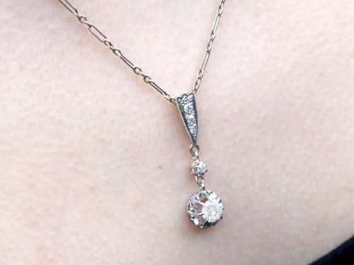 fig 7. An Art Deco platinum drop pendant set with diamonds, featuring a decorative tapered top bail and suspended circular diamond setting on a fine link chain.