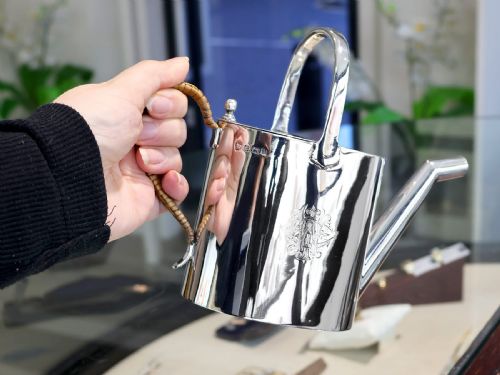 fig 1. An Edwardian sterling silver watering can featuring a cylindrical body, straight spout, overhead loop handle, woven cane side handle, and an engraved central monogram.