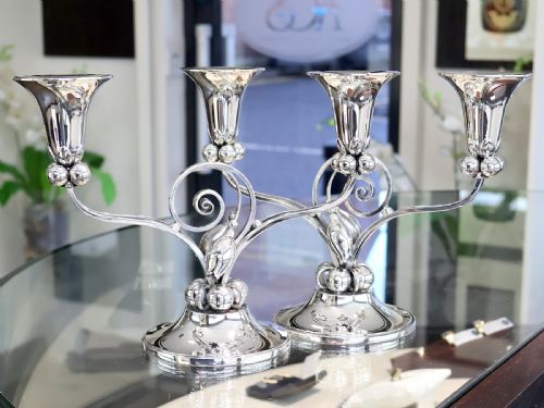 fig 2. A pair of sterling silver two-light Arts and Crafts style candelabra featuring scrolled arms, beaded motifs, and flared sconces on circular bases.