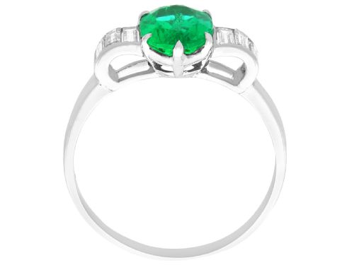 fig 7. An Art Deco platinum dress ring with a central oval green emerald set in claws and flanked by step-cut baguette diamonds on each shoulder.