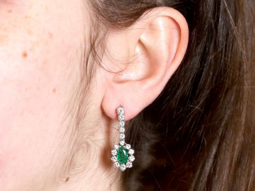 fig 9. A pair of 18ct white gold drop earrings featuring pear-cut green emeralds surrounded by round diamond halos suspended from vertical diamond bars.