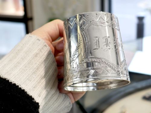 fig 1. A tapered sterling silver christening mug featuring hand-engraved foliage and bird motifs, geometric borders, a loop handle, and a gilt interior.