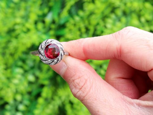 fig 1. An Art Deco platinum dress ring featuring a central round red garnet surrounded by a swirling spiral bezel set with small diamonds.