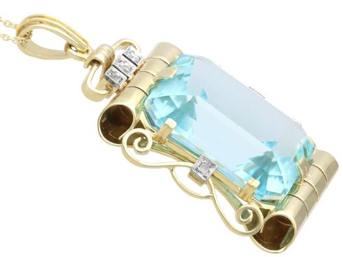 fig 7. A large emerald-cut aquamarine gemstone mounted in a yellow gold scrollwork frame accented with small diamonds and suspended from a chain.