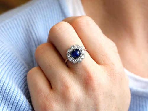 fig 5. A platinum ring set with a central round cabochon blue sapphire surrounded by a halo of ten round diamonds.