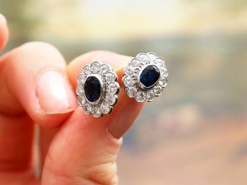 fig 4. Pair of 1930s 18ct white gold cluster earrings featuring oval blue sapphire centerpieces framed by halos of round diamonds.