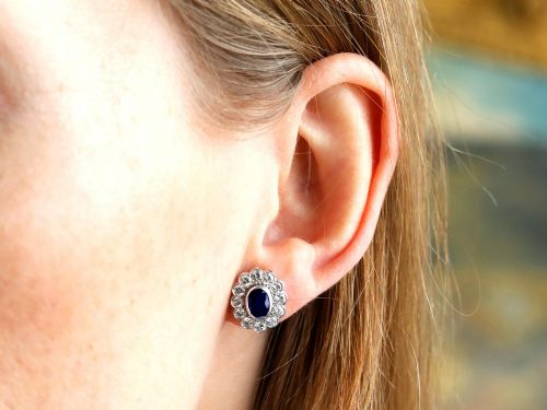 fig 6. Pair of 1930s 18ct white gold cluster earrings featuring oval blue sapphire centerpieces framed by halos of round diamonds.