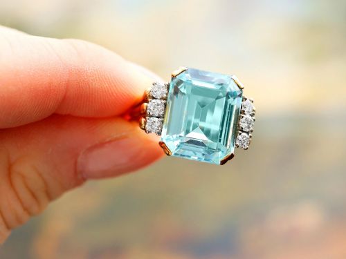 fig 4. A 14ct yellow gold dress ring featuring a large emerald-cut light blue aquamarine central gemstone flanked by six round diamonds.
