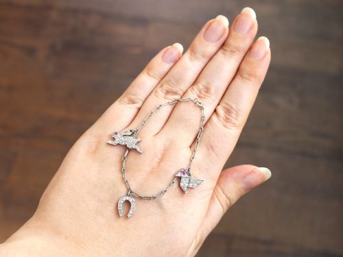 fig 4. An antique platinum link chain charm bracelet featuring diamond-set charms including a running hare, a horseshoe, and a bird with ruby accents.