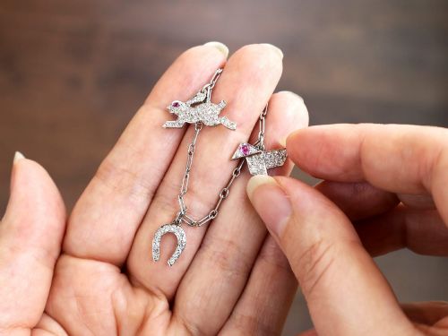 fig 5. An antique platinum link chain charm bracelet featuring diamond-set charms including a running hare, a horseshoe, and a bird with ruby accents.