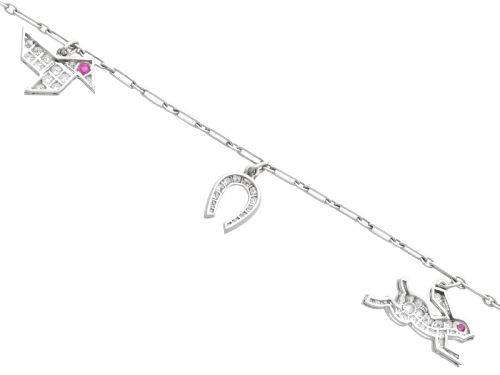 fig 7. An antique platinum link chain charm bracelet featuring diamond-set charms including a running hare, a horseshoe, and a bird with ruby accents.