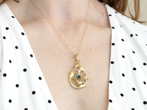 fig 4. An openwork Art Nouveau 14ct yellow gold pendant featuring botanical leaf motifs surrounding a central bezel-set blue sapphire.